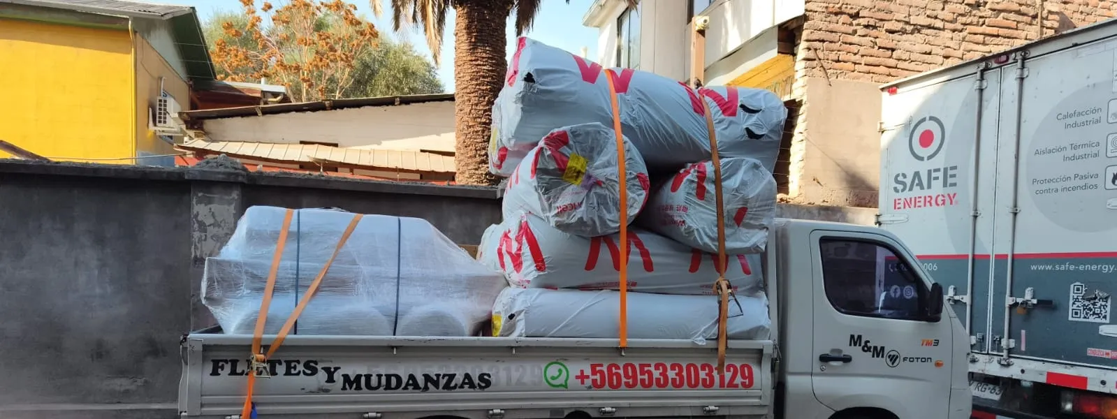 Camión de Fletes Transporte MatCris rotulado, cargado con material de aislación junto al camión de una empresa cliente